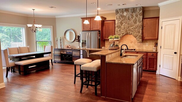 A modern kitchen with wooden cabinets, a stone backsplash, and a central island with bar stools. - Beautiful 5 BR, 3 BA, home only minutes away from the Masters and Peach Jam! (North Augusta)