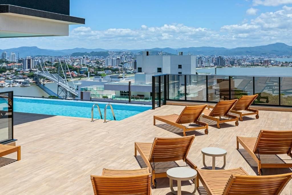 Zona de piscina en la azotea con sillones de madera y vistas a un paisaje urbano y montañas.