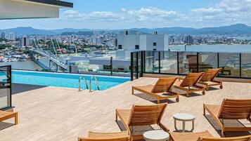 Zona de piscina en la azotea con sillones de madera y vistas a un paisaje urbano y montañas.