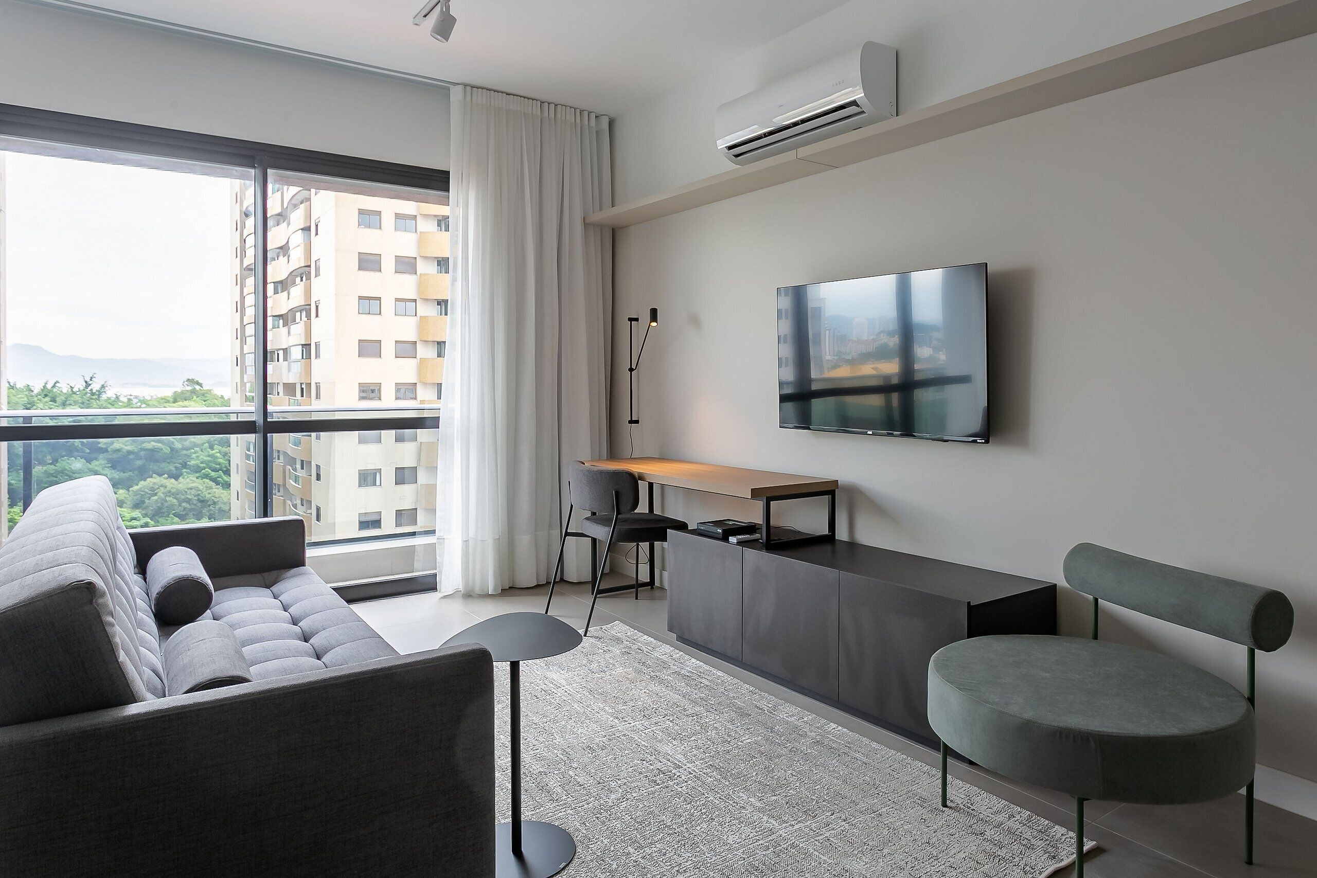 Un salon moderne avec un canapé, un fauteuil rond, un bureau et un téléviseur fixé au mur.