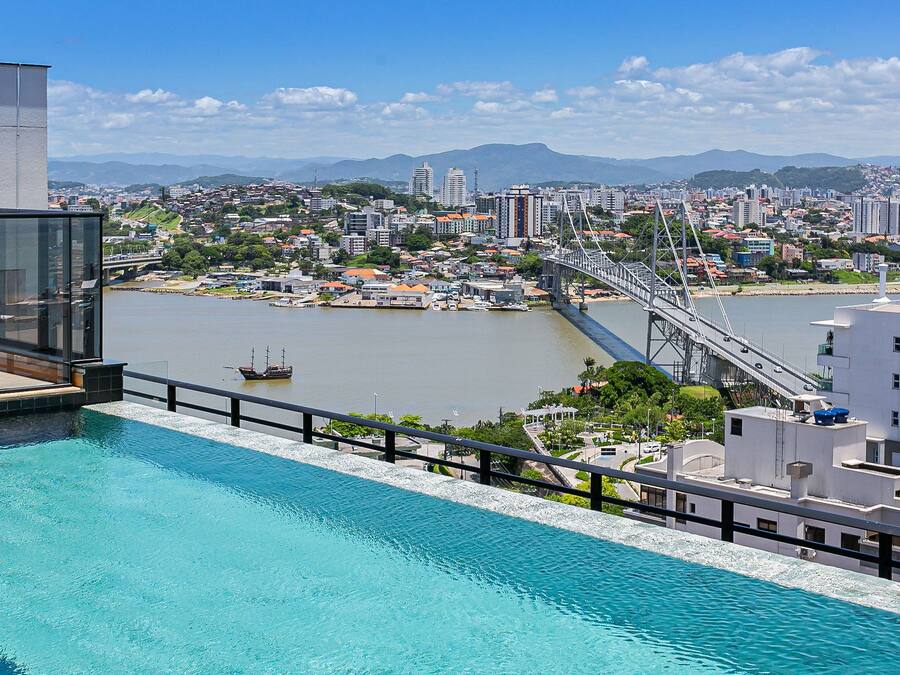 A modern hotel with a rooftop pool overlooking a cityscape, a bridge, and a river.