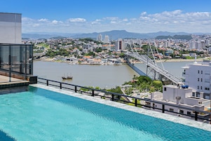 Un hotel moderno con piscina sul tetto e vista sulla città, un ponte e un fiume.