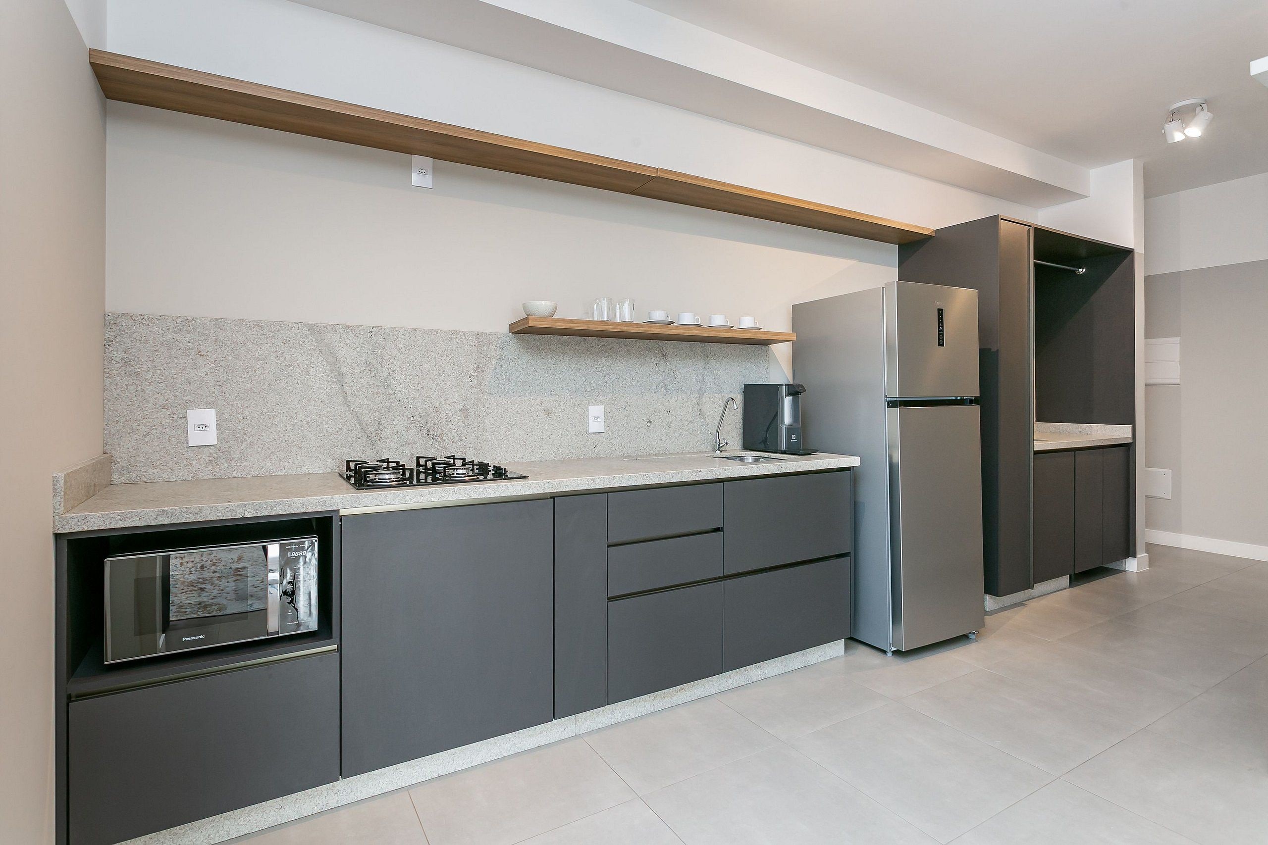 A modern kitchen with a built-in gas stove, a stainless steel refrigerator, and a wooden shelf above the countertop.