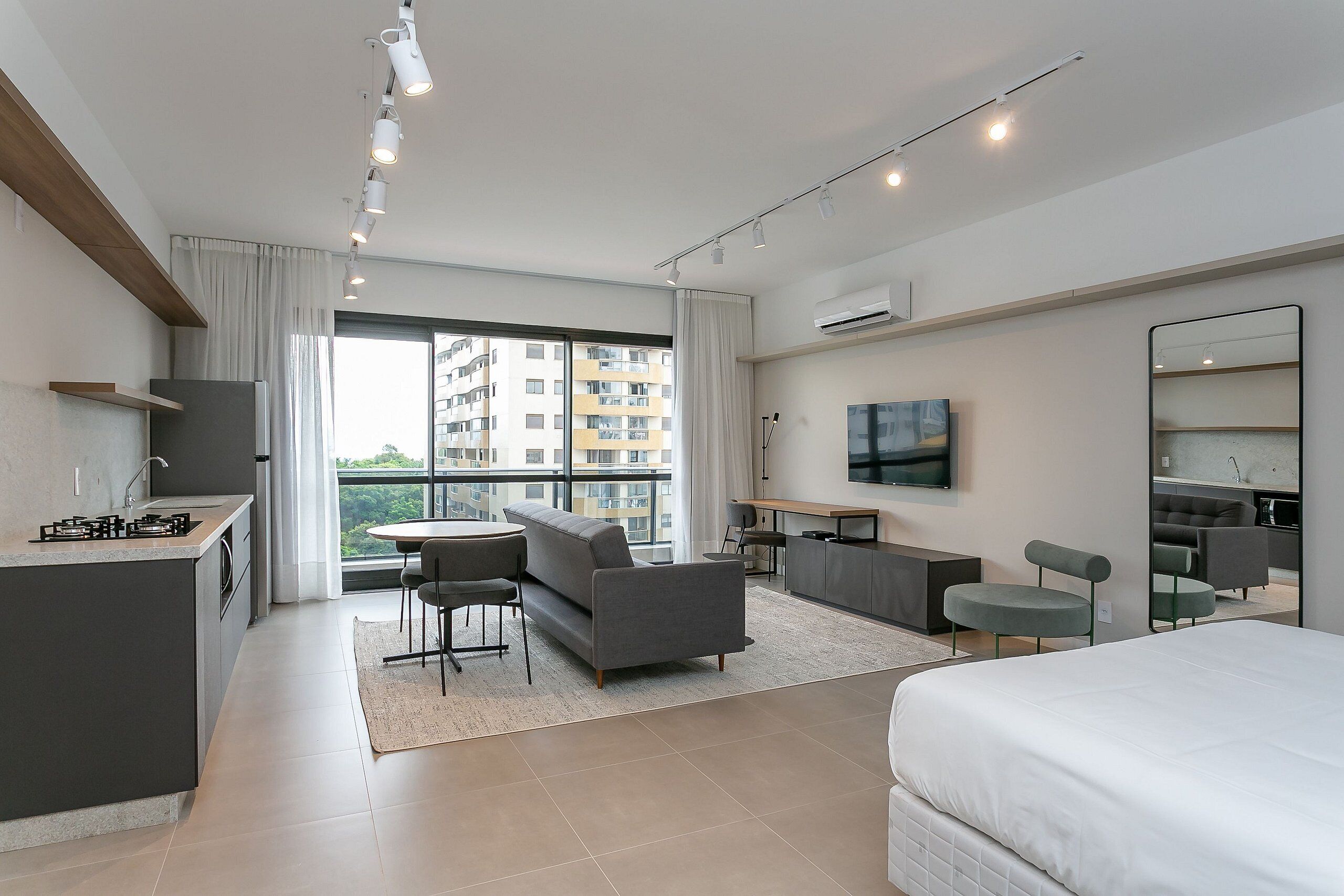 A modern hotel room with a kitchenette, a sofa, a dining area, and a large bed.