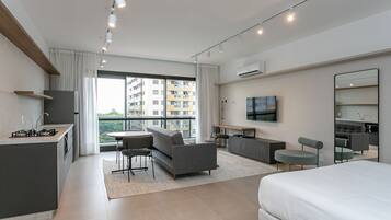 A modern hotel room with a kitchenette, a sofa, a dining area, and a large bed.