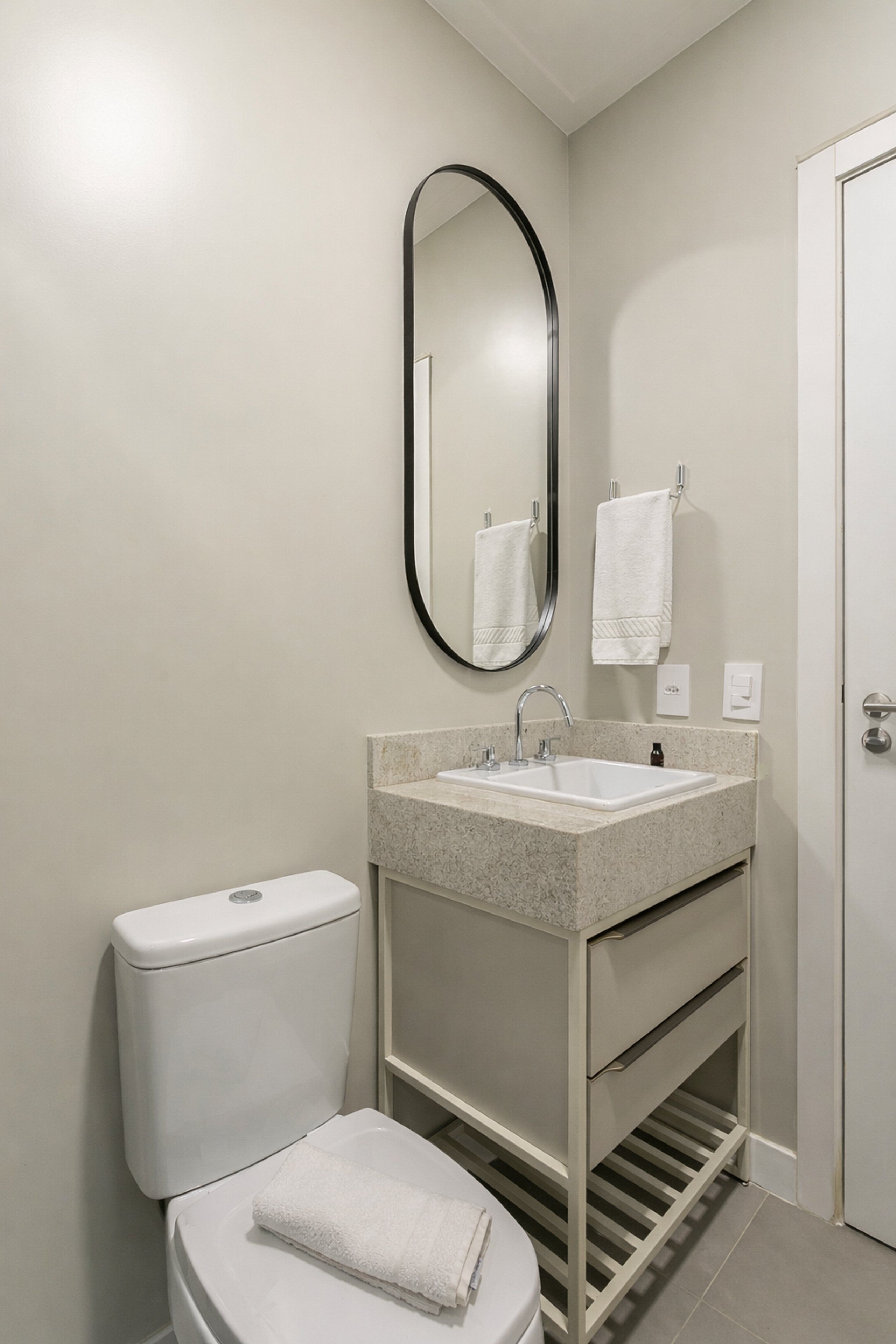 A bathroom with a toilet, sink, mirror, and towel rack.