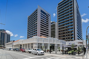 A modern hotel with a covered outdoor seating area, multiple floors, and a clear blue sky.