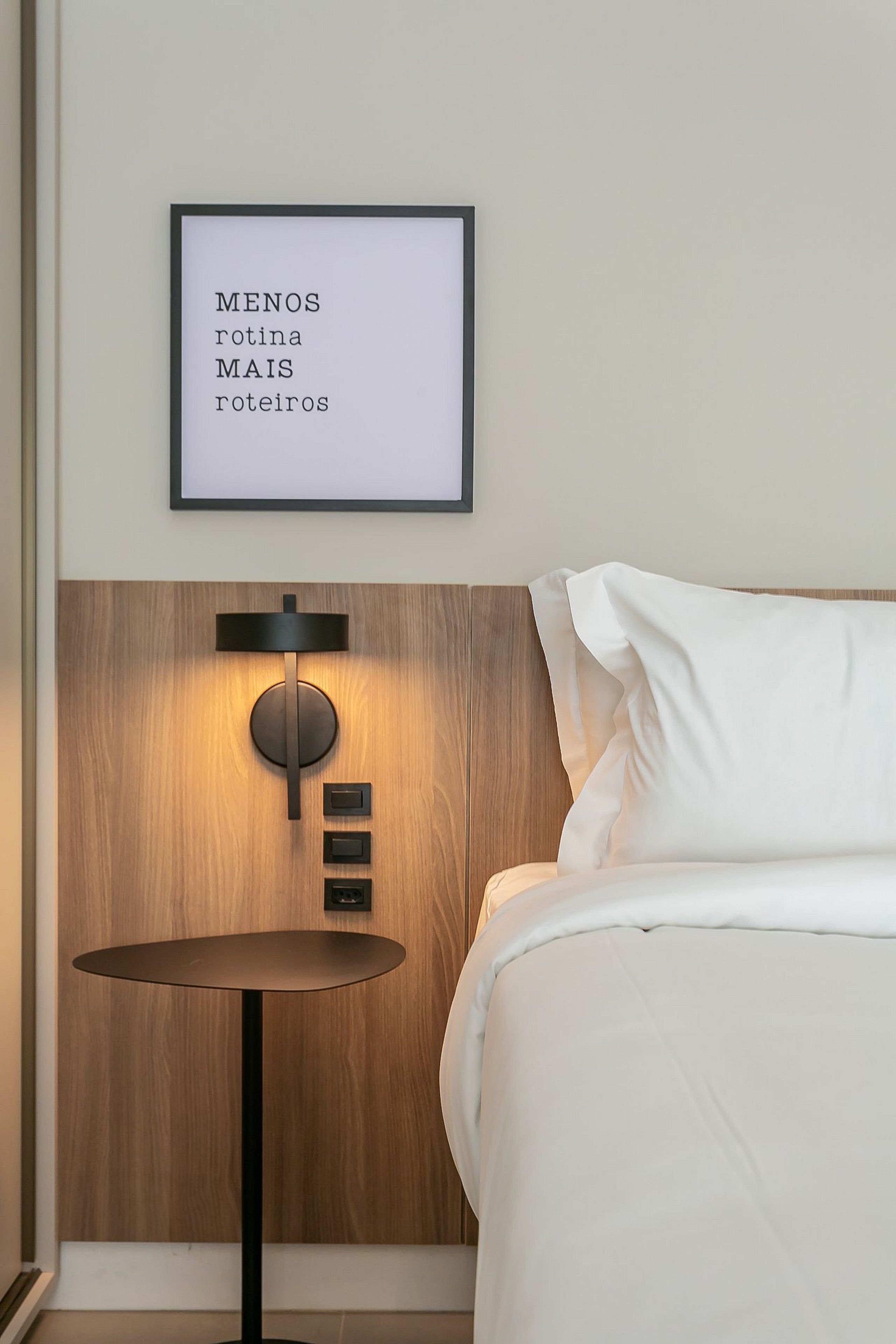 A neatly made bed with white linens, a round table with a black base, and a wall-mounted light fixture.