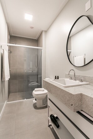 A modern bathroom with a glass-enclosed shower, a white sink, and a toilet. - Studios Tower by Viva - Prédio com piscina no rooftop no centro de Floripa (Florianópolis)