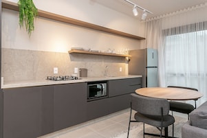 Una cucina moderna con forno a incasso, piano cottura a gas e frigorifero. C'è un tavolo da pranzo con sedie e una pianta sospesa.