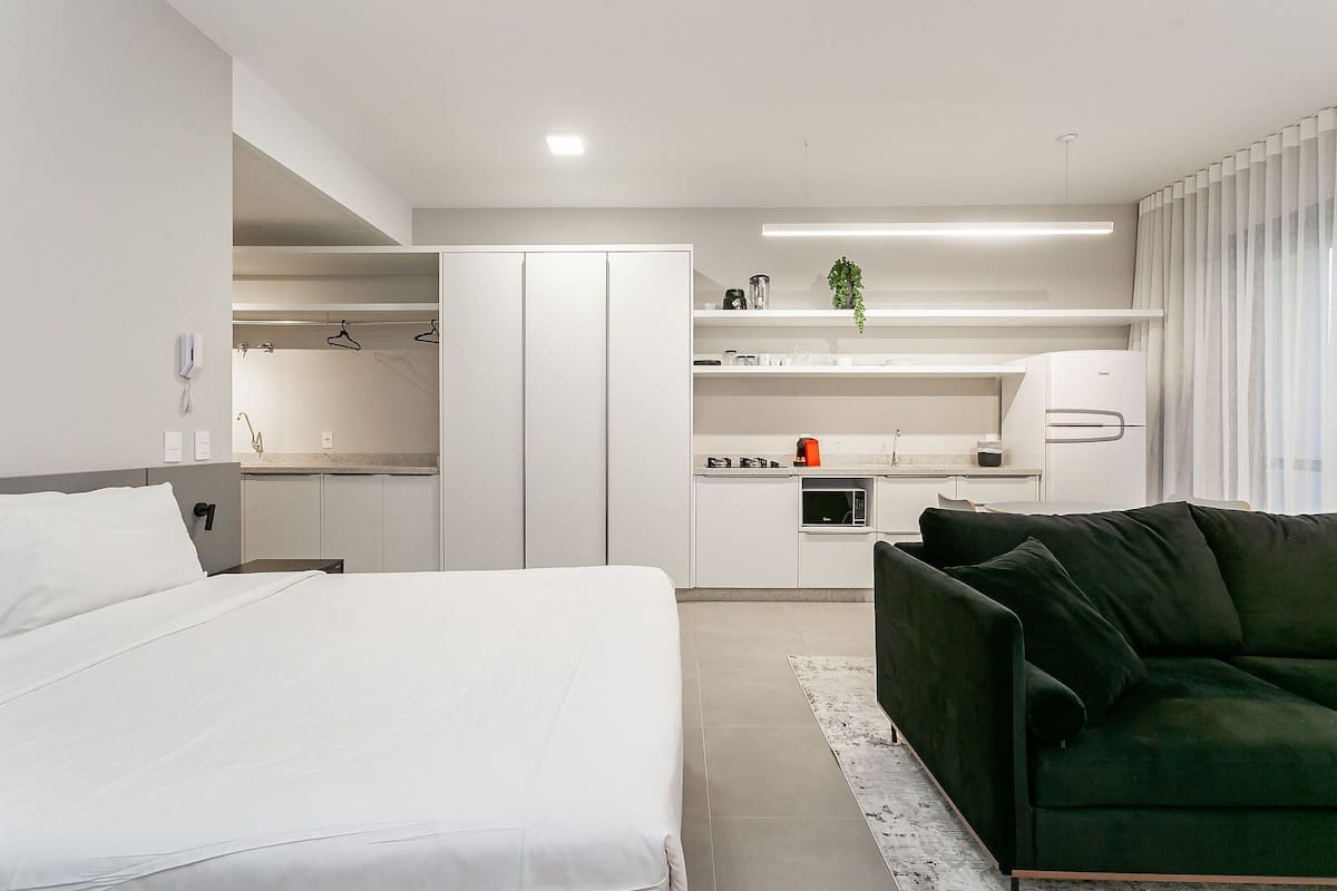 Quarto de hotel moderno com cama, sofá verde, cozinha compacta e closet espaçoso.