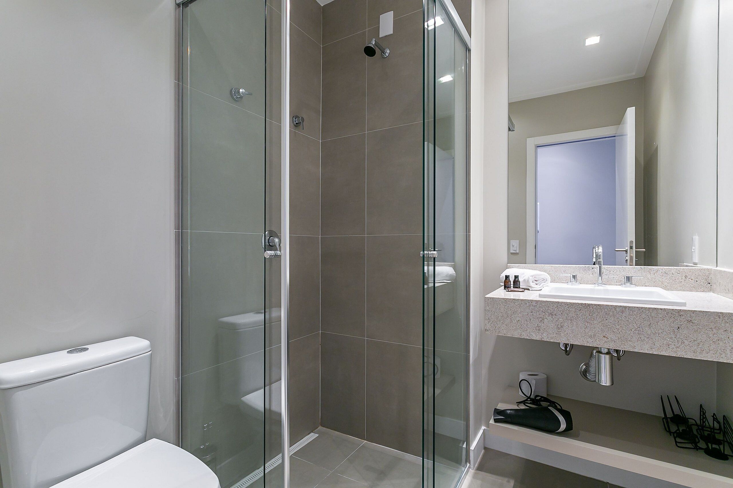 Un baño moderno con ducha de vidrio, inodoro blanco y lavabo con espejo superior.
