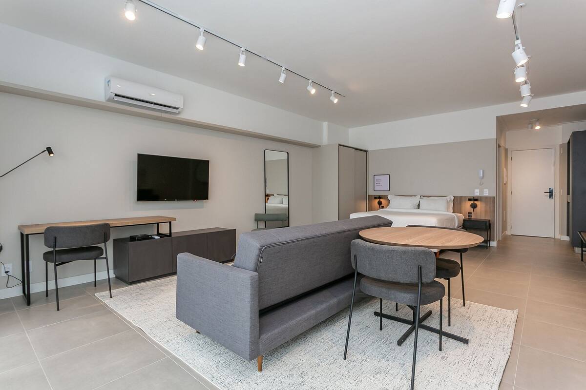 Quarto de hotel moderno com sofá, mesa de jantar, televisão e cama.