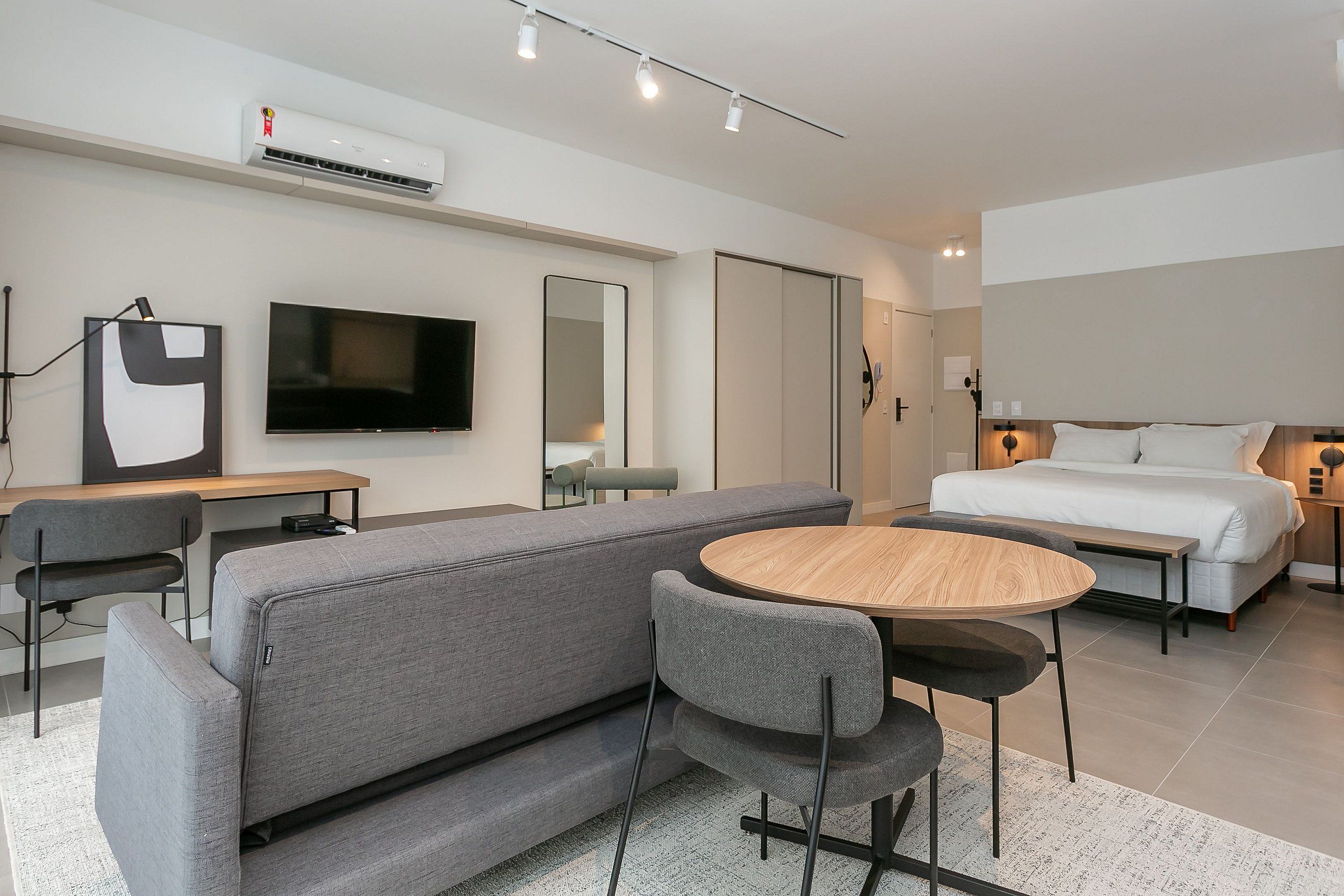A modern hotel room with a sofa, a round table, a bed, a TV, and a wardrobe.