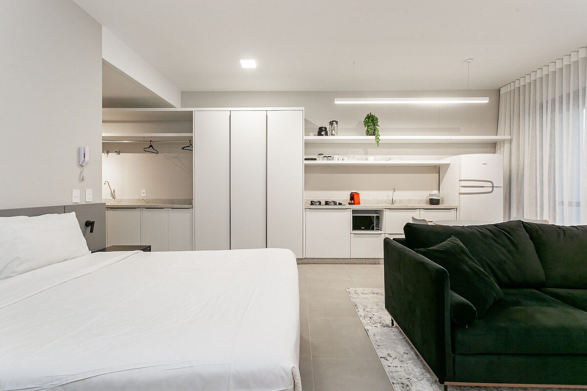 A modern hotel room with a bed, a green sofa, a kitchenette, and a walk-in closet.