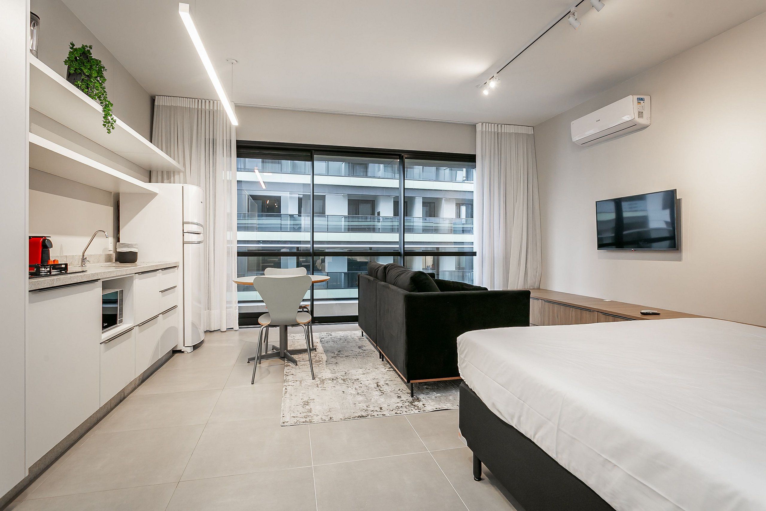 Habitación de hotel moderna con cama, escritorio, sofá y un ventanal con vistas a un edificio.