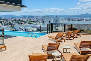 A rooftop pool area with wooden lounge chairs and a view of a cityscape and mountains.