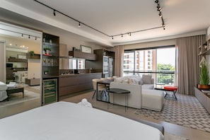 A modern hotel room with a large bed, a dining area, kitchenette, and a balcony with a view of the city. - Studios Tower by Viva - Prédio com piscina no rooftop no centro de Floripa (Florianópolis)