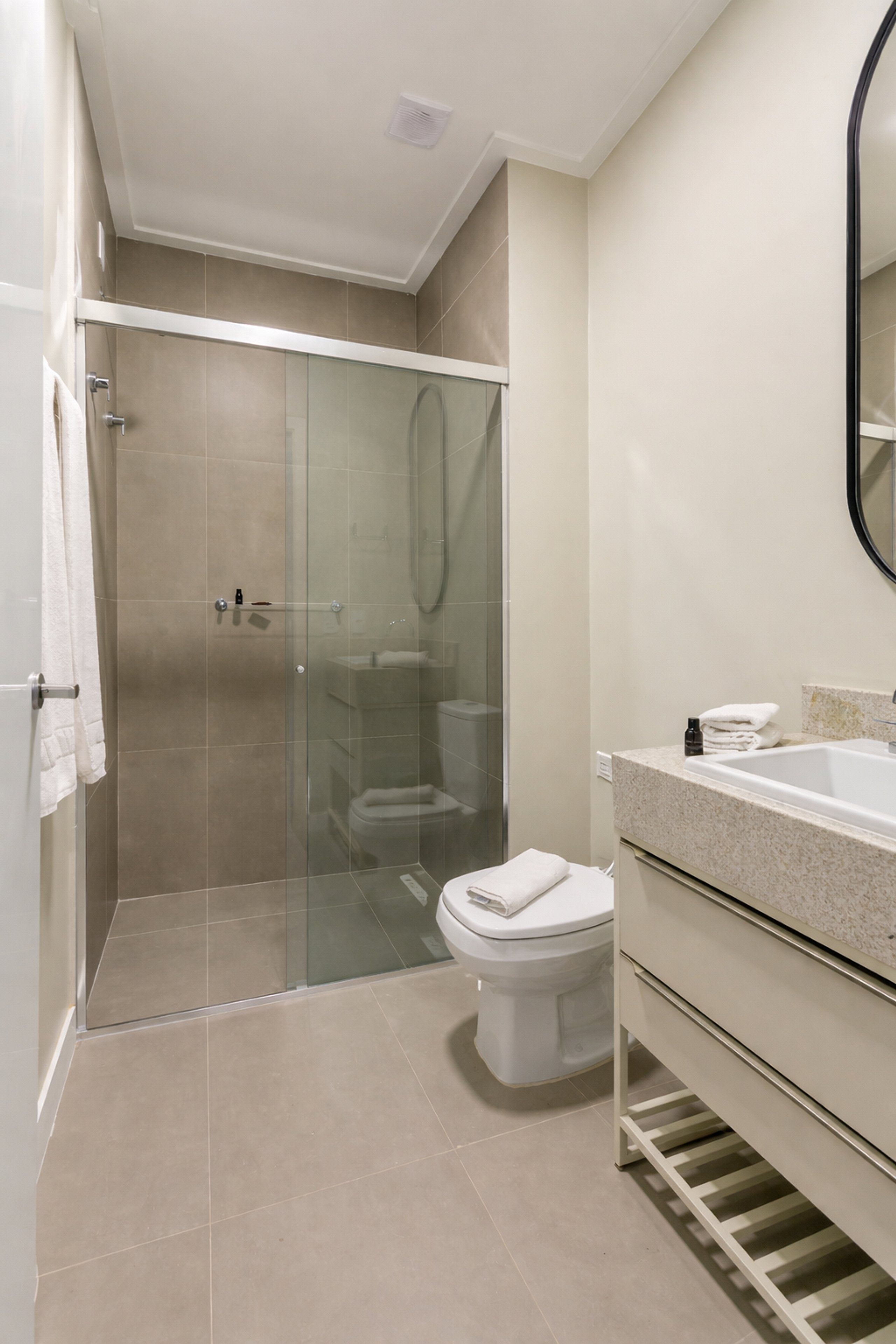 Un baño moderno con ducha acristalada, inodoro y tocador con lavamanos.