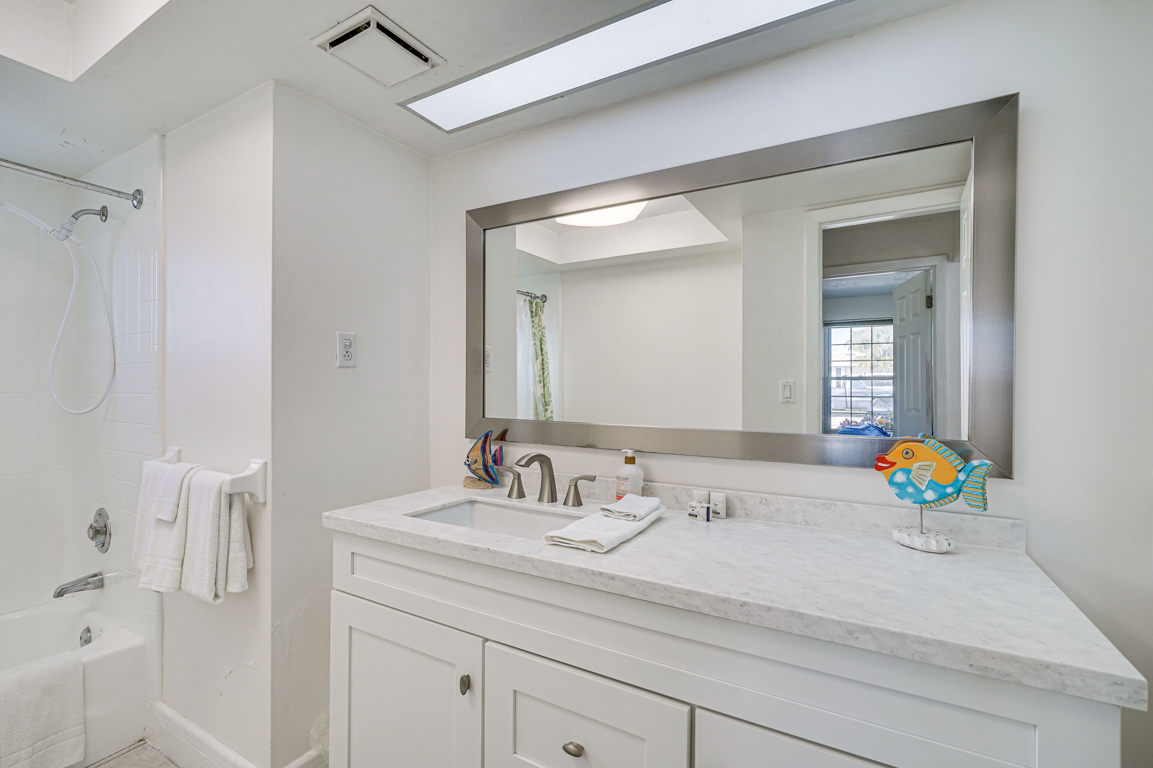 A modern bathroom with a large mirror, white vanity, and a shower area.
