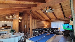 L’intérieur d’une cabane en rondins comprend un coin repas, une table de billard et un téléviseur.