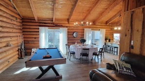 Une charmante cabane en rondins dotée d’une table de billard, d’un coin repas et d’un canapé en cuir.
