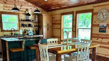 A rustic cabin interior with a wooden ceiling, a kitchen with a central island, and a dining area with a table and chairs.