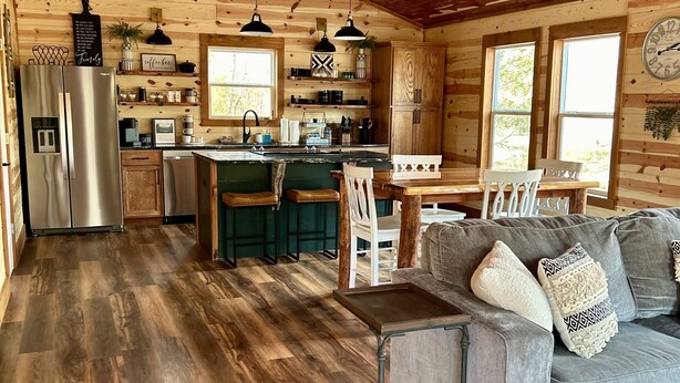 A cozy cabin interior with a wooden interior, a kitchen with a refrigerator, a dining area with a table and chairs, and a living room with a sofa.