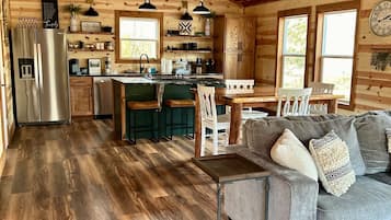 A cozy cabin interior with a wooden interior, a kitchen with a refrigerator, a dining area with a table and chairs, and a living room with a sofa.