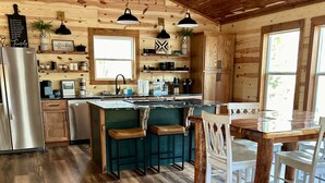 A rustic kitchen with wooden walls, a central island with stools, and a stainless steel refrigerator.