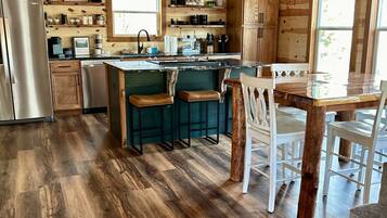 A rustic kitchen with wooden walls, a central island with stools, and a stainless steel refrigerator.