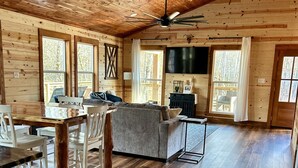 A spacious wooden cabin interior with a dining area, living room, and large windows.