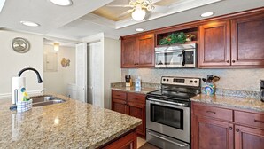 Una cocina con encimeras de granito, armarios de madera, electrodomésticos de acero inoxidable y un ventilador de techo.