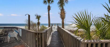 A wooden boardwalk leading to a beach with palm trees and beach chairs.