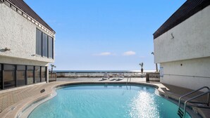 Una piscina con muelle de madera, vista al océano y una valla que separa la piscina de la playa.