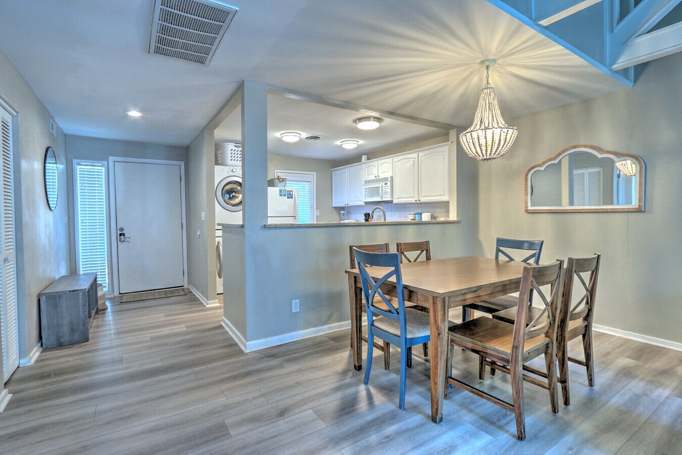 A modern kitchen with white cabinets, a dining area with a wooden table and blue chairs, and a chandelier.