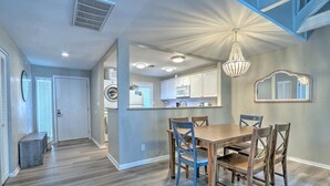 A modern kitchen with white cabinets, a dining area with a wooden table and blue chairs, and a chandelier.