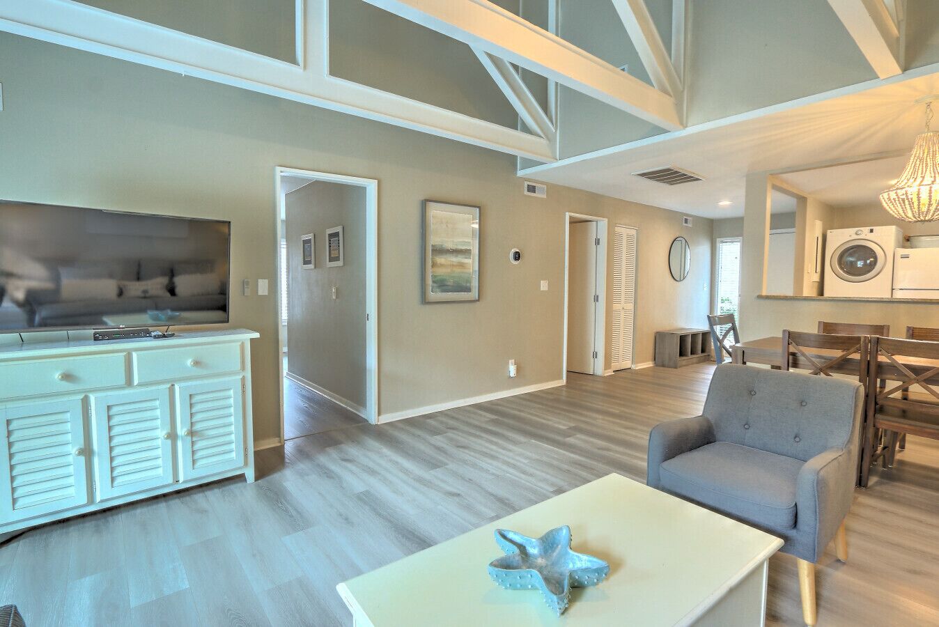 A spacious living area with a flat-screen TV, a coffee table with a starfish decoration, and a dining area with wooden furniture.