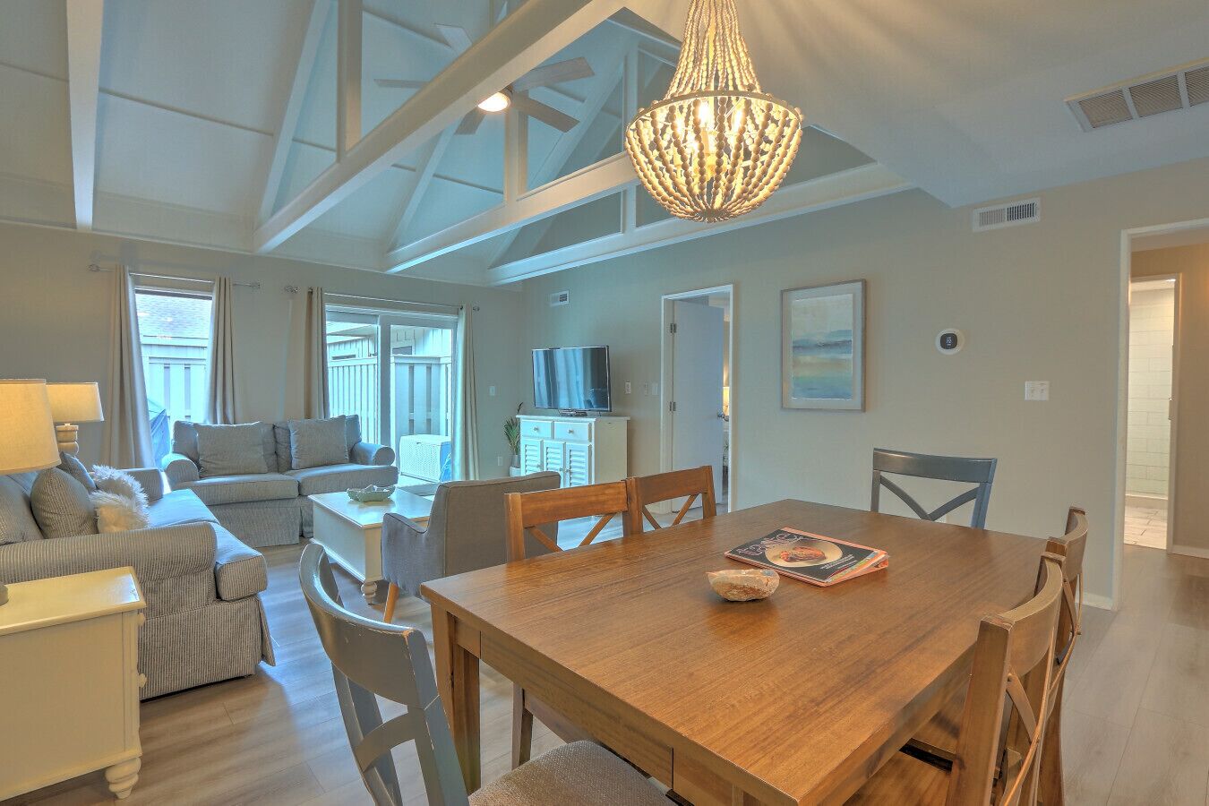A spacious living area with a wooden dining table, comfortable seating, a television, and a large window.