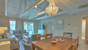 A spacious living area with a wooden dining table, comfortable seating, a television, and a large window.