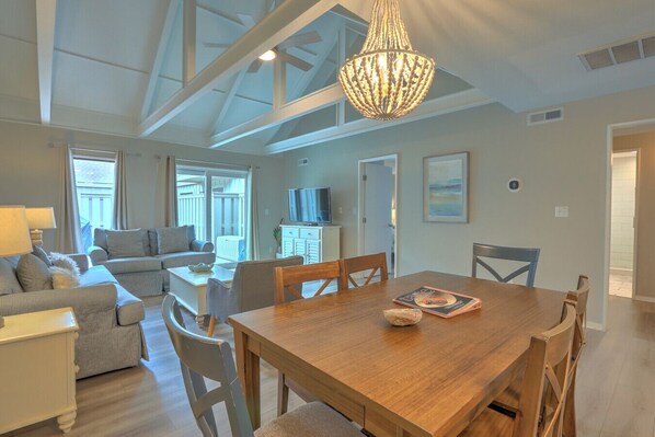 A spacious living area with a wooden dining table, comfortable seating, a television, and a large window.