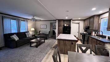 A modern living room with a dark-colored sofa, a coffee table, and a dining area with a wooden table and chairs.
