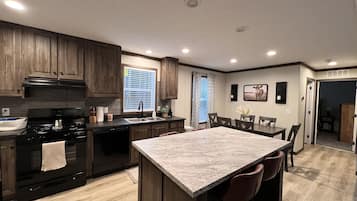 Une cuisine moderne avec des meubles de couleur bois foncé, une cuisinière noire et un îlot en marbre agrémenté de tabourets de bar.