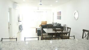 Un salon moderne avec un canapé, une table à manger et des chaises. On y trouve également un ventilateur de plafond et une horloge au mur.