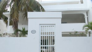 A white building with a gated entrance, a balcony, and a palm tree.