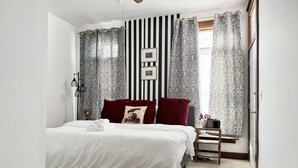 Een slaapkamer met een bed, nachtkastje, gordijnen, een plafondventilator en een wandlamp.