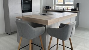 A modern kitchen with a central island, two grey chairs, and a built-in oven. - Vollausgestattete Wohnung im Neubau (Waldshut-Tiengen)