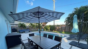 Une terrasse avec une piscine, du mobilier d’extérieur et un parasol.