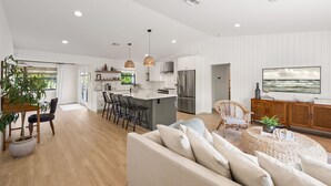 A spacious living area with a large sofa, a dining table with chairs, a kitchen with a central island, and a television mounted on the wall. - Shorebird Cottage - heated pool - 1 mi from beach (Bonita Springs)