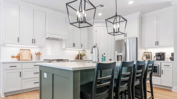 Una cocina moderna con armarios blancos, una isla central con taburetes altos e iluminación colgante.